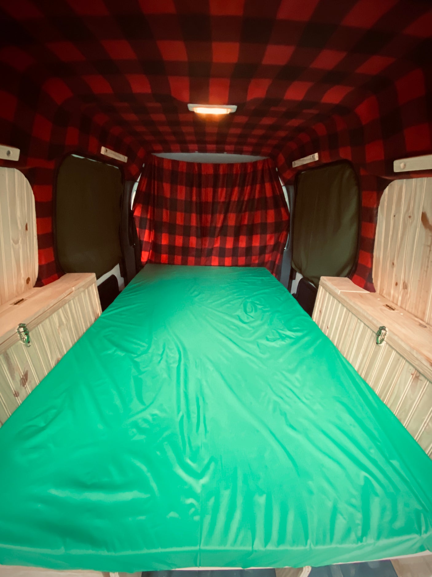 RV rental camper van interior with red plaid ceiling, large green mattress, and wooden storage benches.