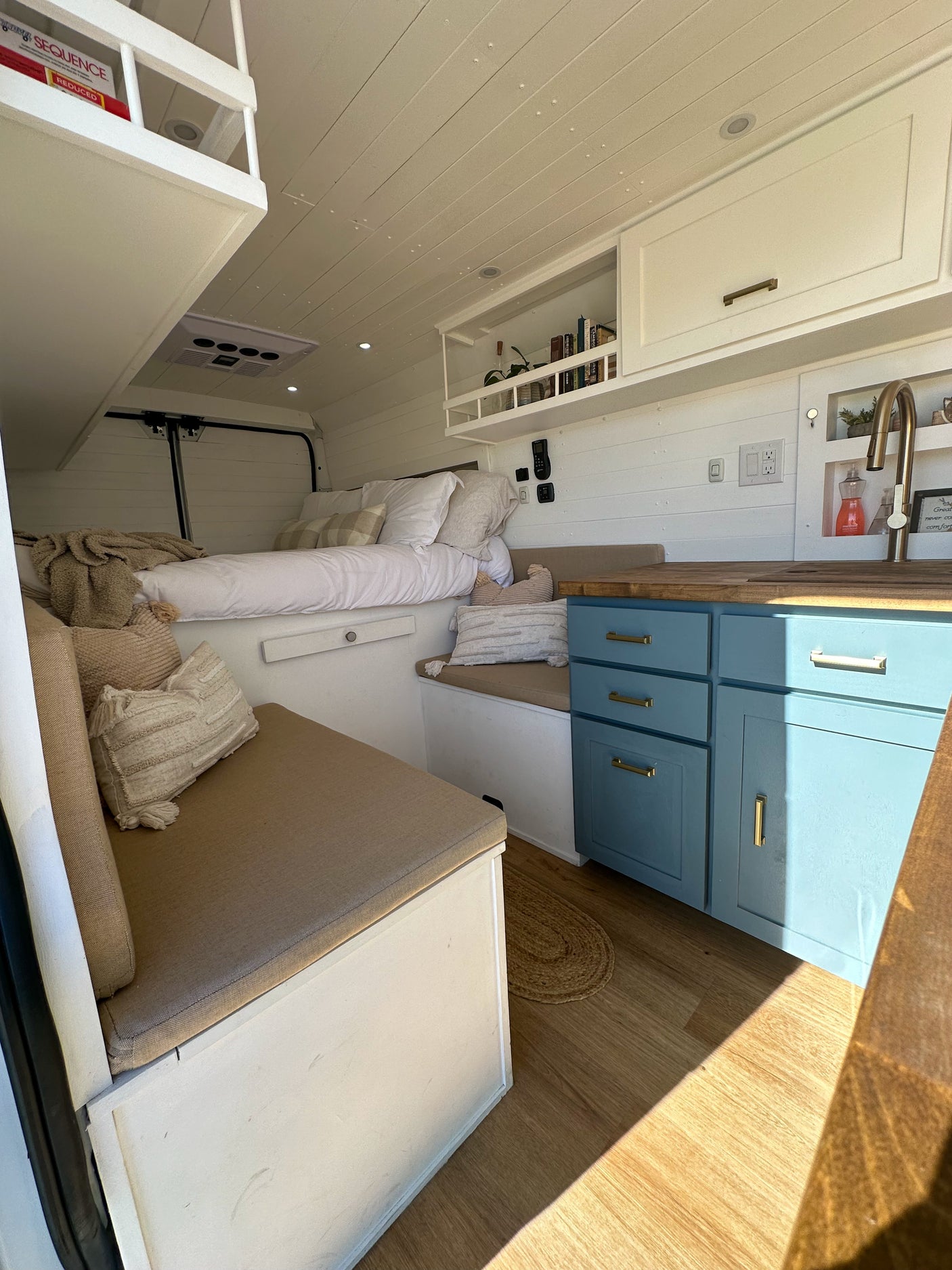 This RV rental offers a charming interior: comfy bed, compact kitchen with blue cabinets & wood counters, and cozy seating.