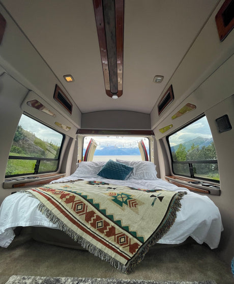 Cozy rv rental interior featuring a comfy bed with a patterned blanket and stunning mountain & lake views out the back.