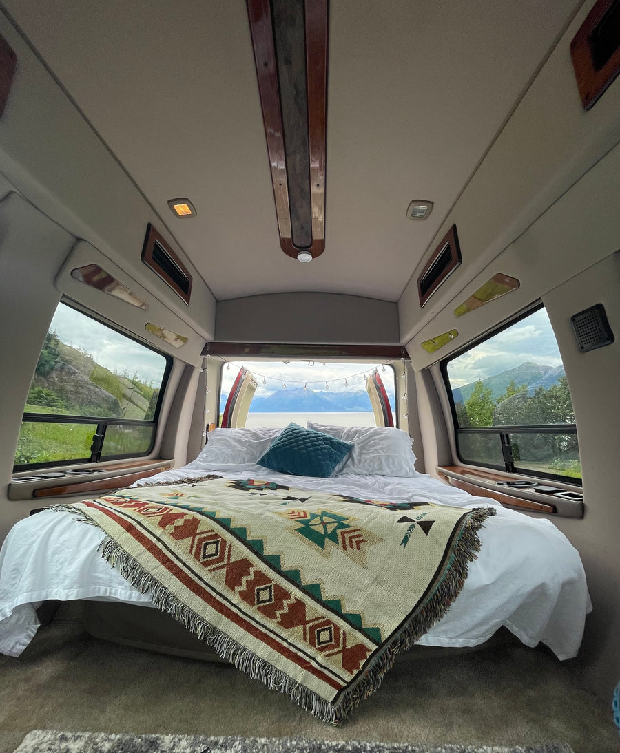 Cozy rv rental interior featuring a comfy bed with a patterned blanket and stunning mountain & lake views out the back.