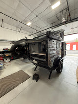 This rugged off-road camper trailer, perfect for rv rental adventures, is open in a workshop, showing its storage.