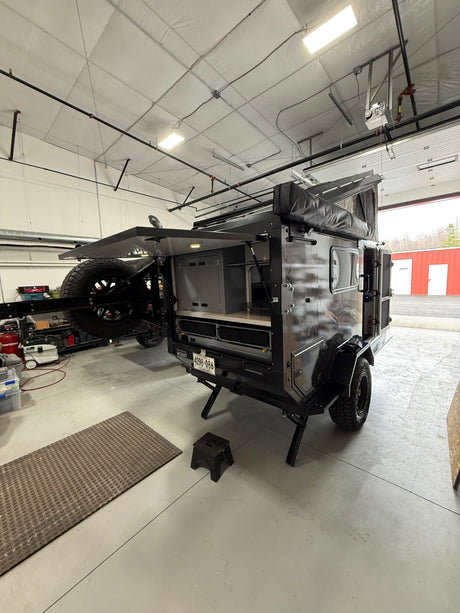 This rugged off-road camper trailer, perfect for rv rental adventures, is open in a workshop, showing its storage.