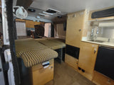 View inside an RV rental, showing a multi-section bed/seating area, kitchen with sink, and light wood cabinetry.