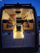 Bright, cozy custom RV rental interior with comfy bench seating, a versatile table, and ambient floor lighting.