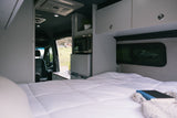 Experience an RV rental: interior with a cozy bed, compact kitchen (microwave, fridge), and driver's cab.