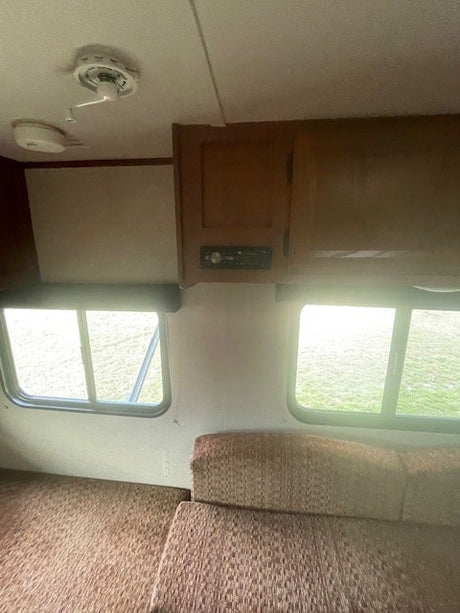 Inside an RV rental: cozy living space with brown seating, large windows, and overhead cabinets with a stereo. Ideal for travel.