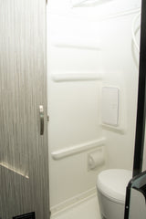 Inside an RV rental: a compact, bright white bathroom features a toilet, shower, and integrated shelves for convenience.