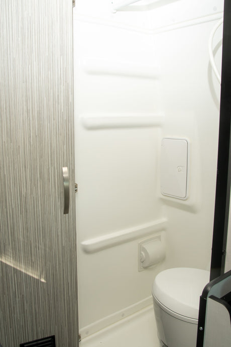 Inside an RV rental: a compact, bright white bathroom features a toilet, shower, and integrated shelves for convenience.