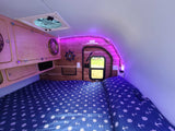 Cozy RV rental interior with nautical bedding, wood accents, and ambient purple LED lighting.