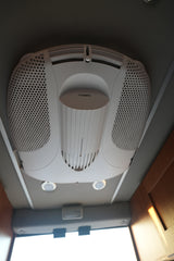 Overhead Dometic air conditioning unit in an rv rental, with perforated grilles, central vent, and ceiling lights.