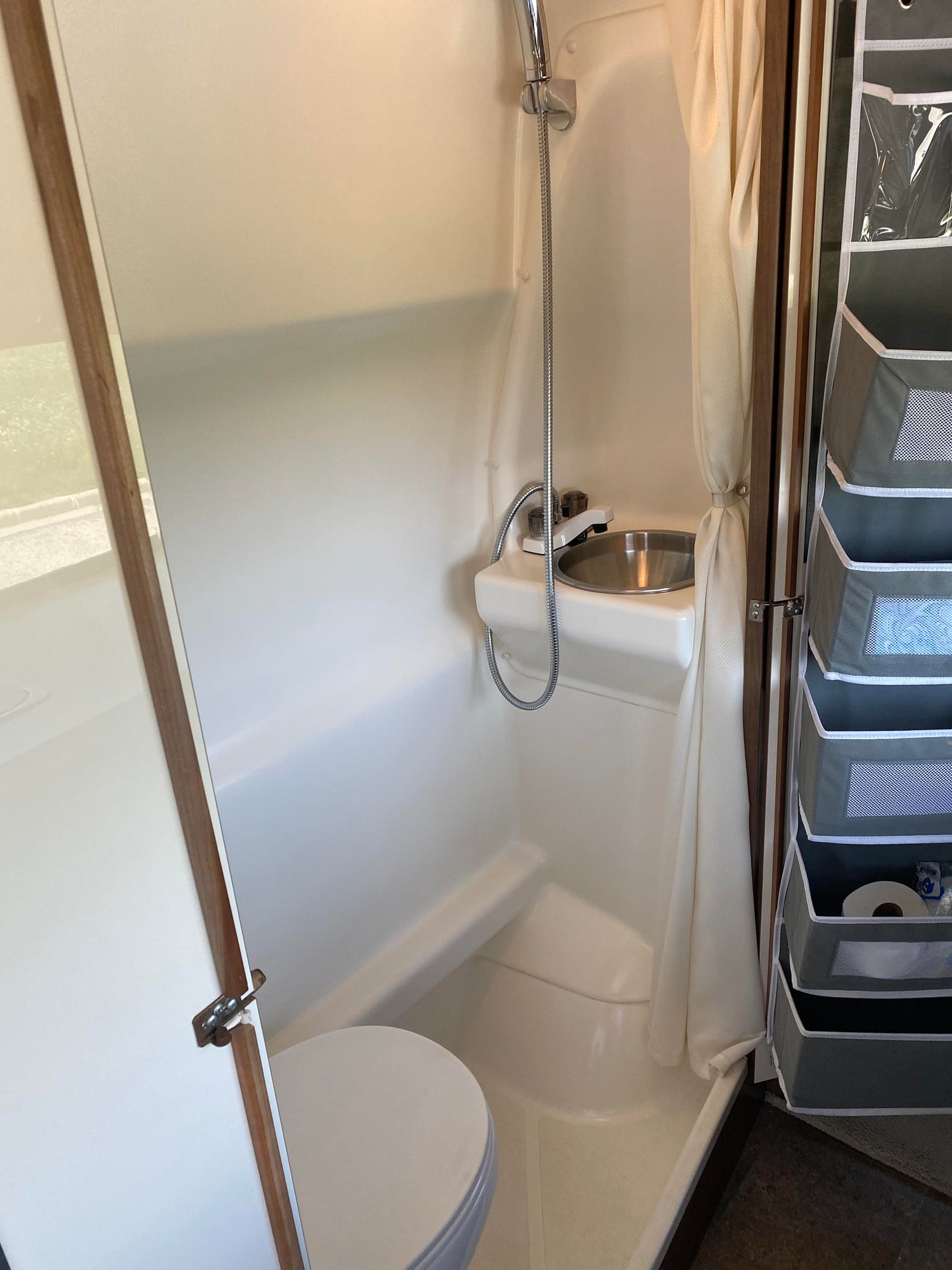 An RV rental's compact wet bath showing a white toilet, small sink, shower, and hanging storage organizer.