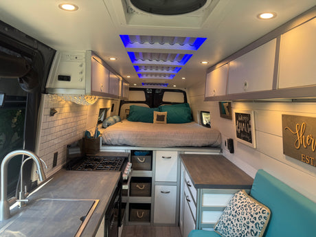 Bright, modern RV rental interior with full kitchen, raised bed, and stylish storage. Ideal for comfortable travel.