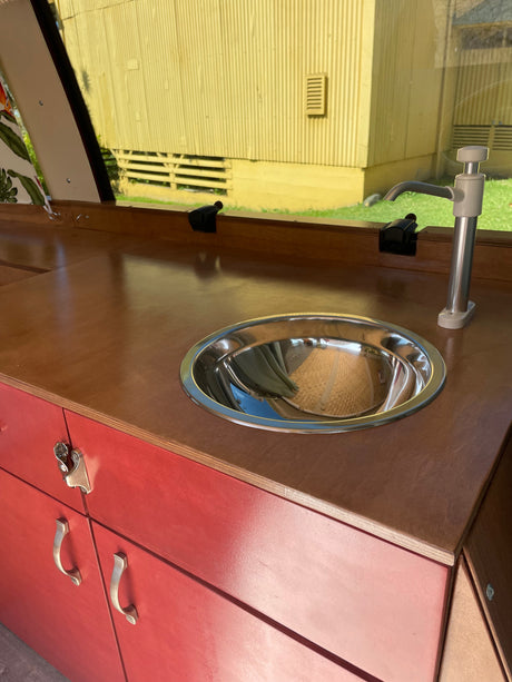 RV rental: A compact camper kitchen with a wooden counter, stainless steel sink, pump faucet, and red storage cabinets.