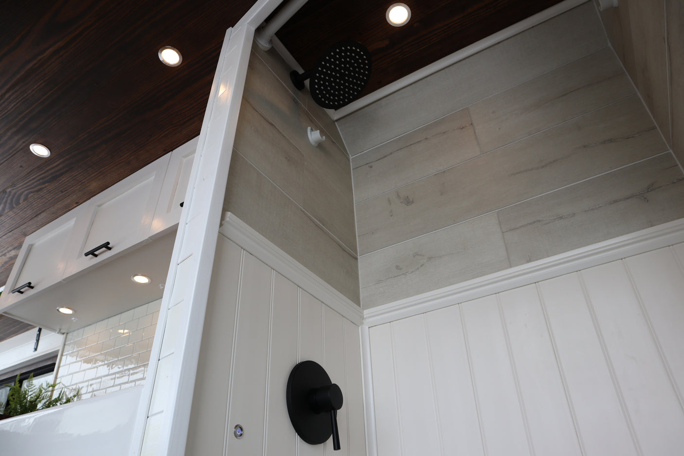 Stylish RV rental interior showcasing a modern shower with grey wood-look tiles, black fixtures, and a warm wood plank ceiling.