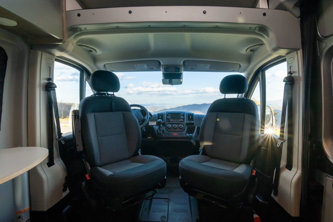 Inside an RV rental: front cabin with comfortable seats, dashboard, and a clear view of beautiful mountains ahead.