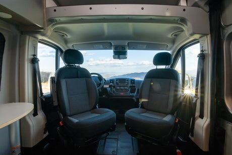 Inside an RV rental: front cabin with comfortable seats, dashboard, and a clear view of beautiful mountains ahead.