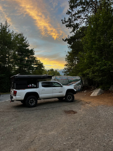 Sunset over Maine! This equipped Toyota Tacoma RV rental is ready for adventure near a painted "Keep Maine Beautiful" rock.