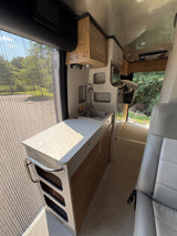 Step inside this modern RV rental featuring a kitchen with a sink, cabinetry, and a large window with a bug screen.