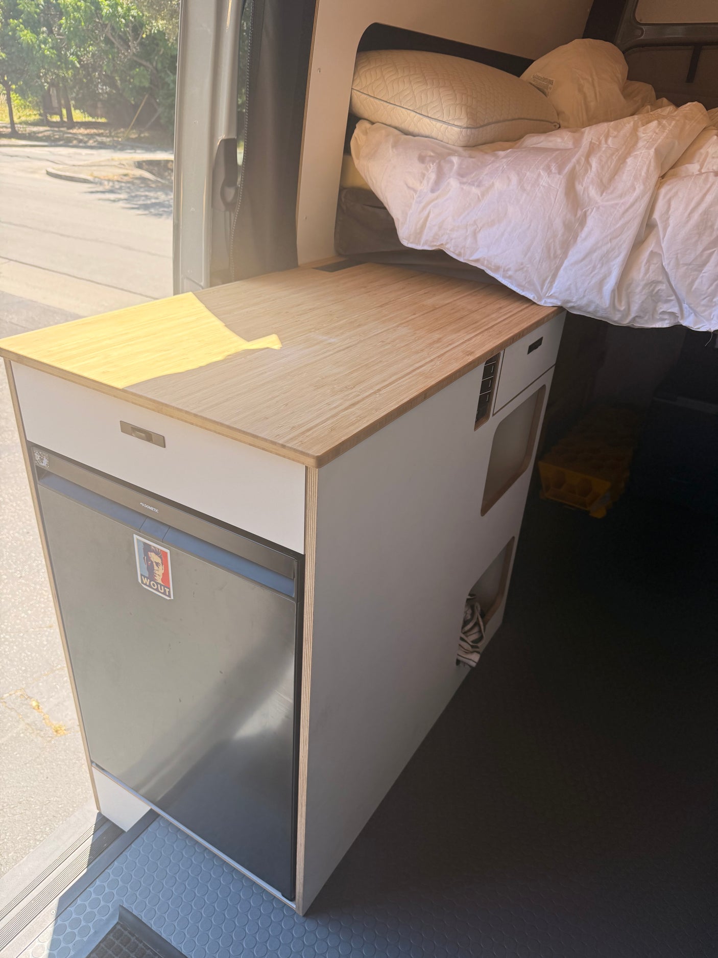 Cozy RV rental campervan interior with a compact kitchen, Dometic fridge, wooden counter, and a comfortable bed.
