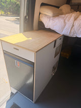 Cozy RV rental campervan interior with a compact kitchen, Dometic fridge, wooden counter, and a comfortable bed.