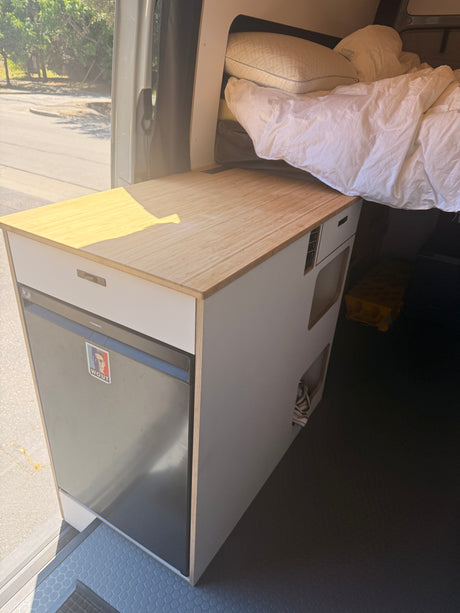 Cozy RV rental campervan interior with a compact kitchen, Dometic fridge, wooden counter, and a comfortable bed.