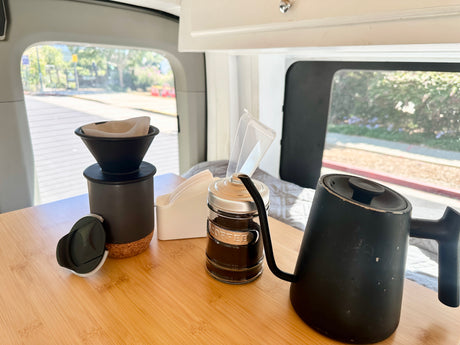 Pour-over coffee setup on a wooden table inside an RV rental, with kettle, filters, and grounds visible.