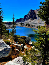 Explore this serene mountain lake with rocky shores & majestic peaks, framed by evergreens. Your RV rental adventure!