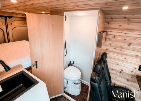 Inside a modern RV rental: wood-paneled interior with a comfy bed, functional sink, and private wet bath with toilet/shower.