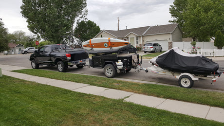 Outdoor enthusiast's dream: Black truck with bikes, an RV rental adventure trailer carrying a paddleboard, and a jet ski.