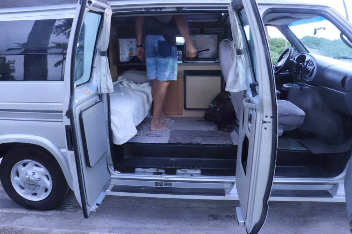 Inside an rv rental camper van: person by kitchen & bed, open doors reveal comfy living space & front cab. — photo 19