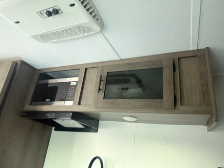 RV rental kitchen with modern overhead cabinets, built-in microwave, and range hood. An AC unit is on the ceiling.