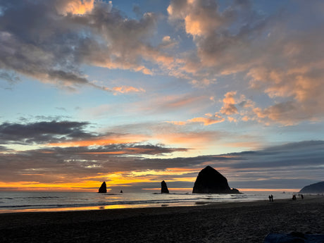 Golden sunset illuminates sea stacks on a sandy beach. A stunning Oregon coast view, ideal for an RV rental adventure.