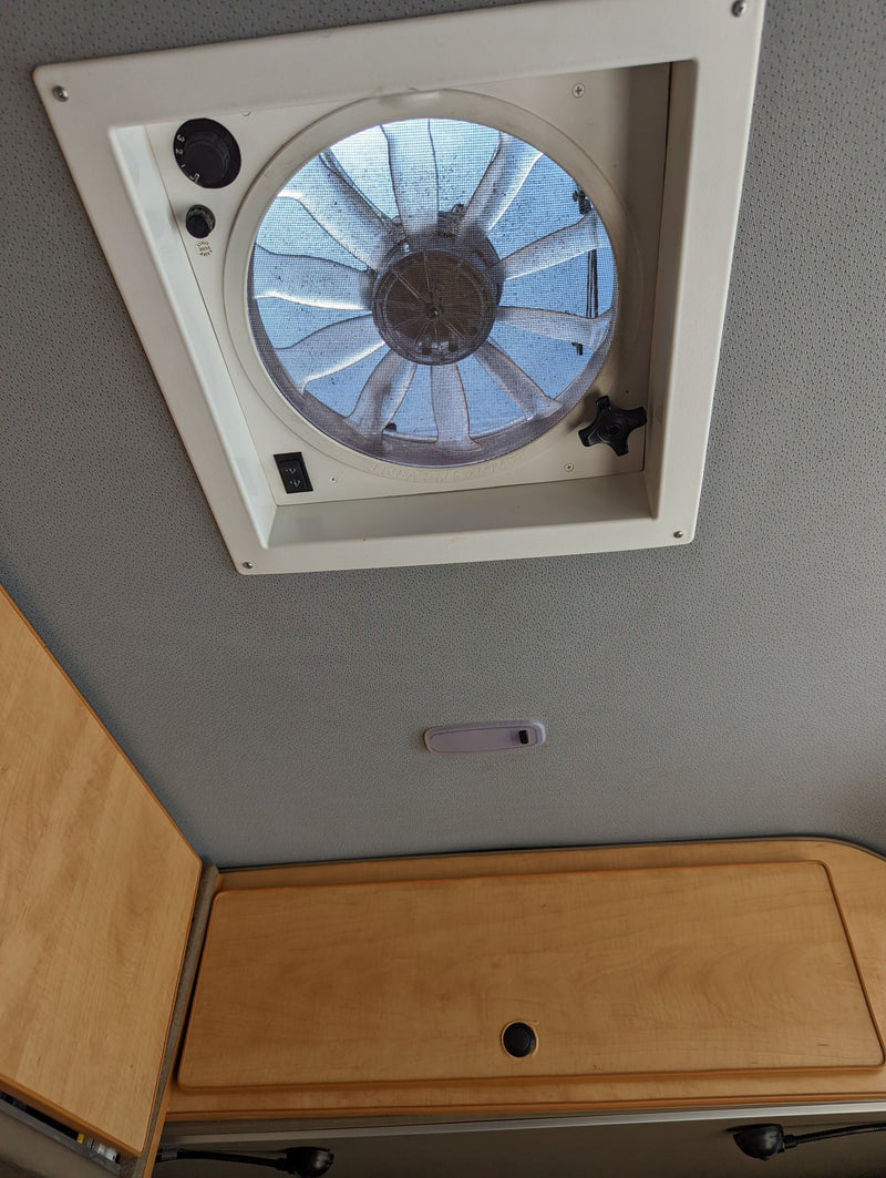 Experience comfort in your RV rental with this ceiling fan, its controls, overhead light, and wooden storage cabinets. — photo 16