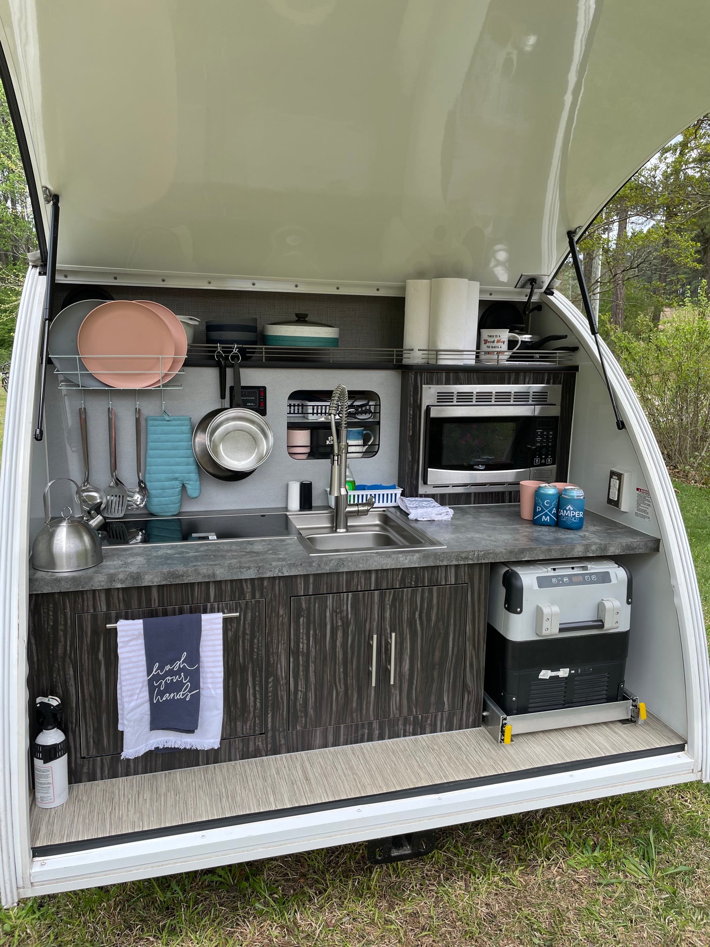 This RV rental's compact outdoor galley features a sink, microwave, fridge, and storage, perfect for camping.
