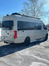This light-colored Mercedes Sprinter camper van, ready for rv rental, is parked on a sunlit, icy lot under a clear sky.