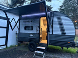 Evening view of a cozy SUN LITE LTD travel trailer rv rental, door open with interior lights on and awning extended with LED strip lighting.
