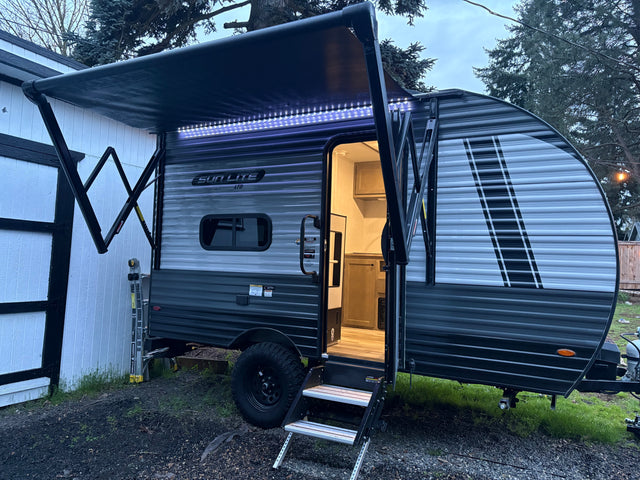 Evening view of a cozy SUN LITE LTD travel trailer rv rental, door open with interior lights on and awning extended with LED strip lighting.