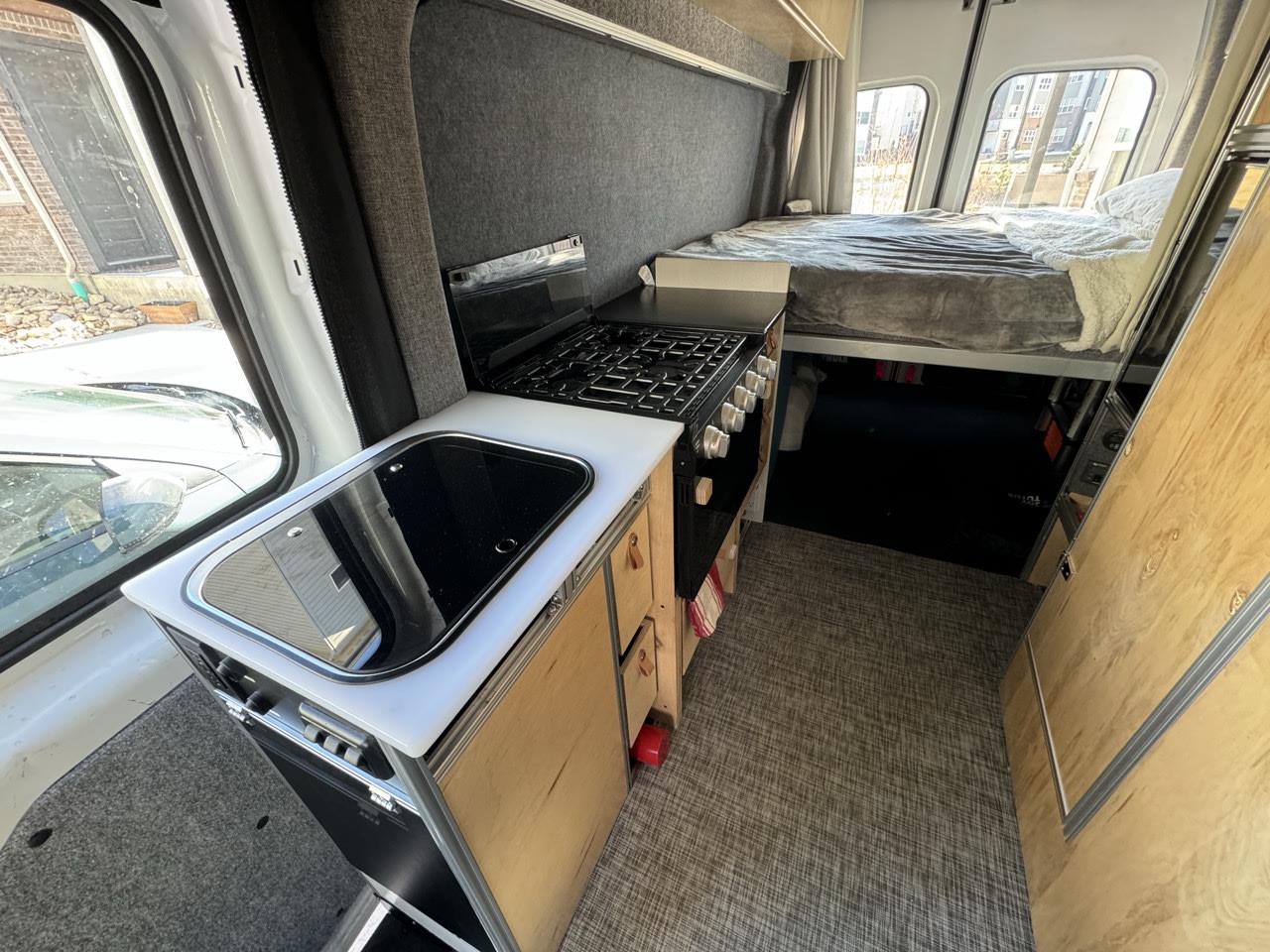 Inside an RV rental: a modern camper van interior featuring a kitchen with stove & sink, plus a comfy elevated bed.