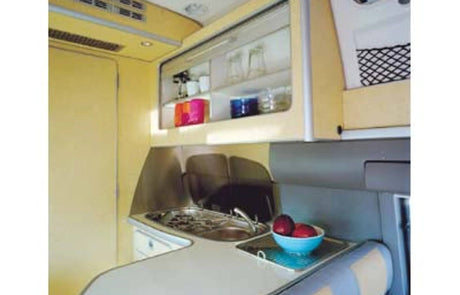 Explore this RV rental's efficient galley kitchen. Features include a sink, stovetop, and overhead cabinets with bright tableware.