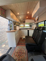 RV rental: Inside a modern converted camper van with a wood ceiling, kitchen, bed, and comfortable passenger seating.