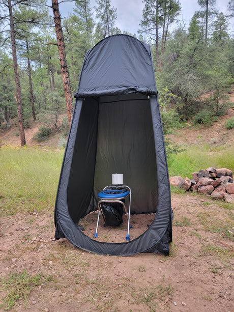 Black camping privacy tent houses a blue portable toilet with paper, ideal for RV rental trips.