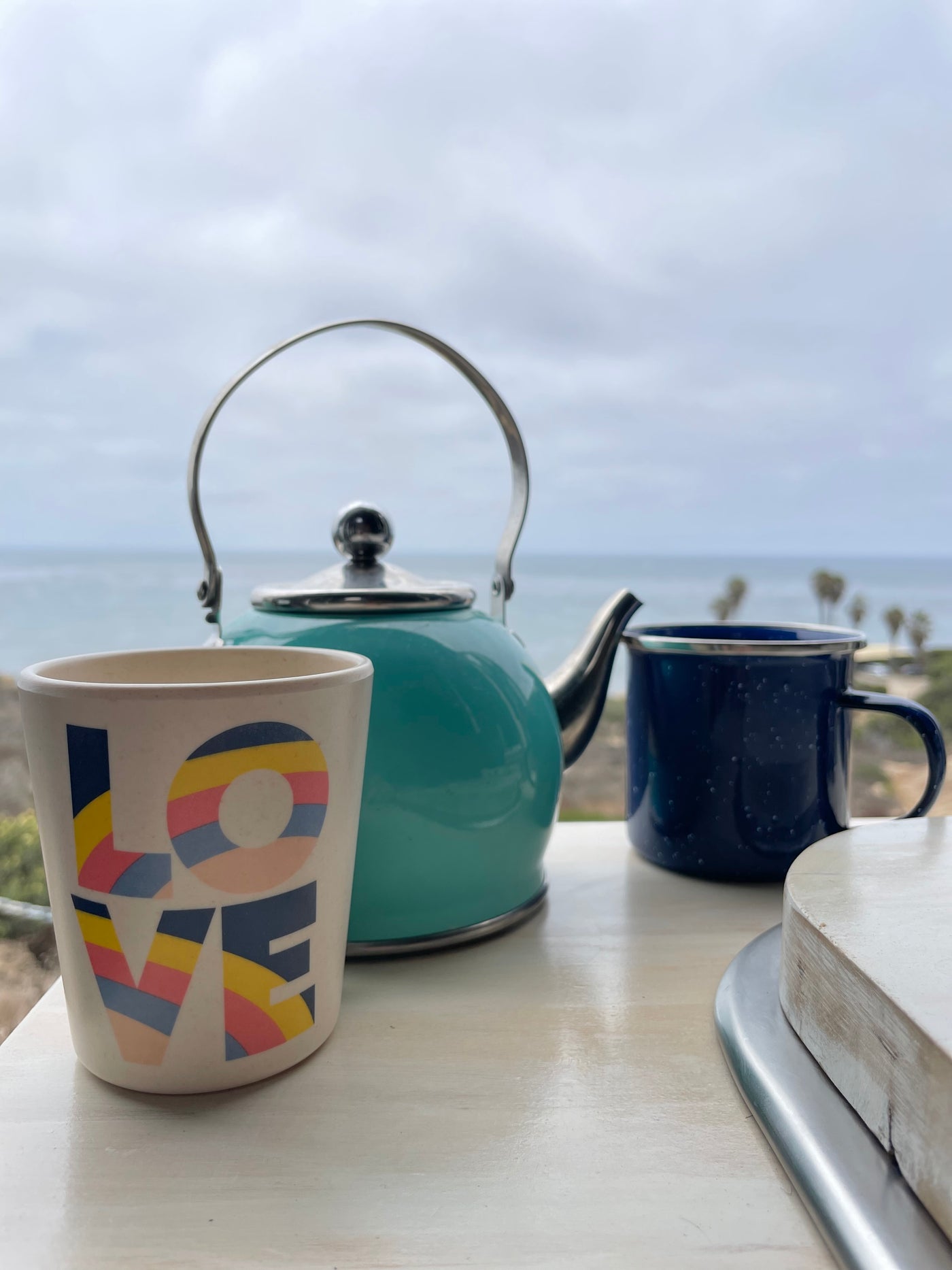 Enjoying a serene ocean view from an RV rental with a turquoise kettle and two mugs, one with "LOVE" and a blue enamel. — photo 15