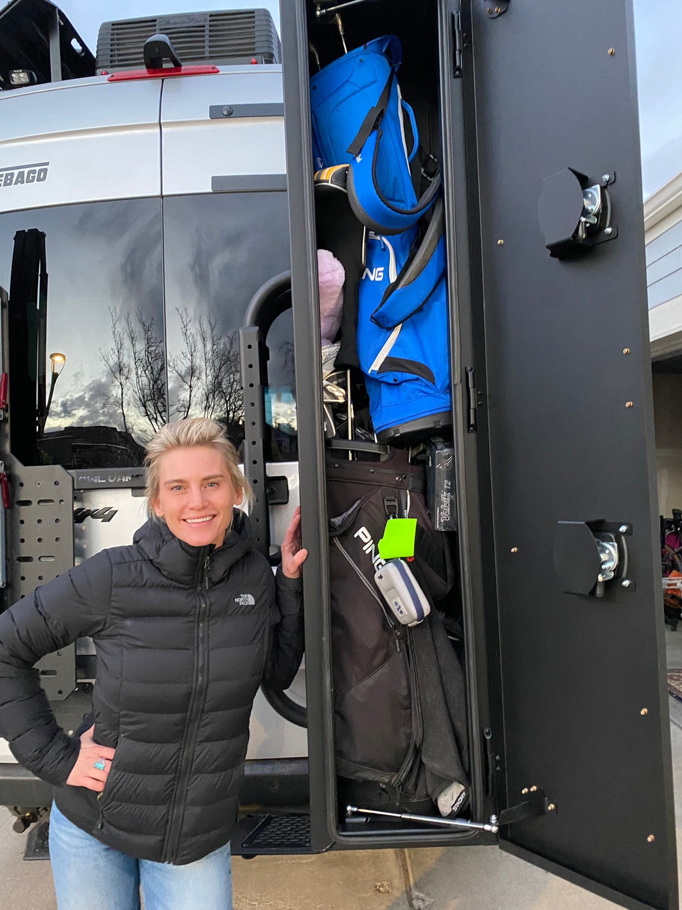 Winnebago RV rental with custom Owl Vans golf storage. A woman stands proudly beside the open locker of golf bags.