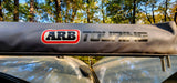 ARB Touring awning on an RV rental, reflecting sunlit trees. Essential gear for outdoor adventures.