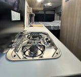 rv rental interior: A detailed view of the compact kitchen with a two-burner stove, sink, and comfortable bed.
