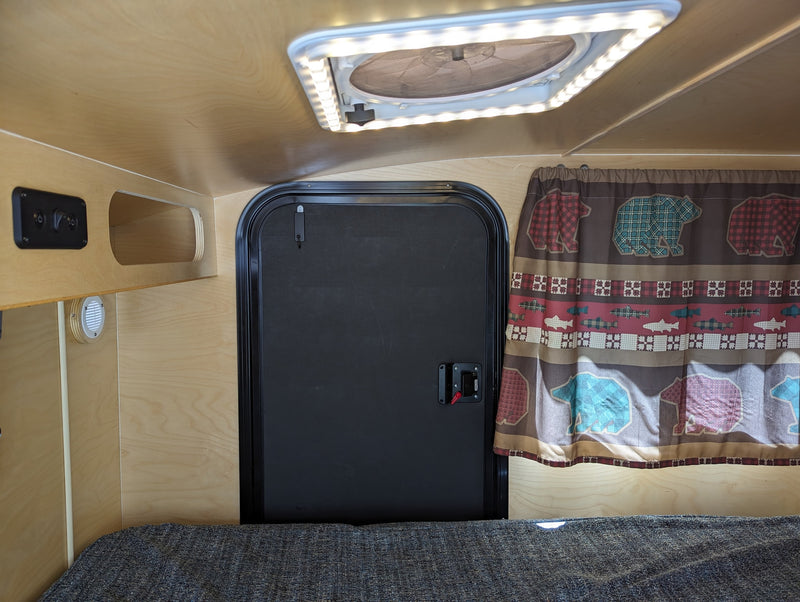  and campfire on a black background.|NOCO RV rental charging port showing a male electrical inlet with three pins.|View inside a compact RV rental: wood-paneled interior — photo 4