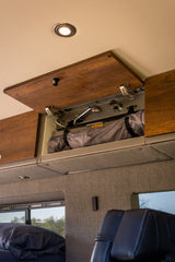 Explore this RV rental's interior: an open overhead cabinet reveals a portable shower system and stored gear, maximizing space.