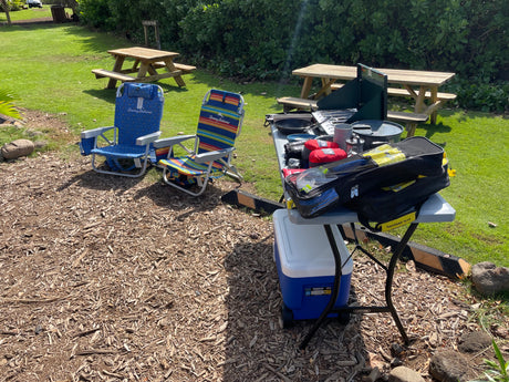 An RV rental provides this perfect outdoor setup: chairs, cooler, cooking gear, and a dive bag at a grassy campsite.