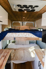Cozy RV rental interior featuring wooden ceilings, bunk beds with plush bedding, and compact camper van design.