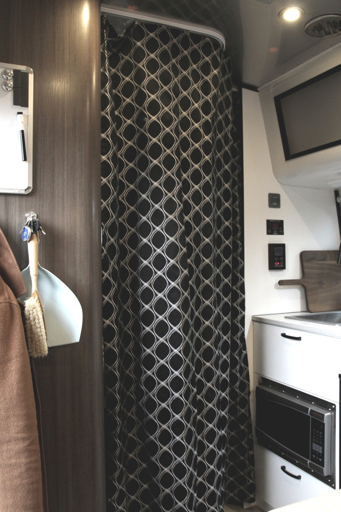 Compact RV rental interior showing a black patterned shower curtain, kitchen sink, and built-in microwave unit.
